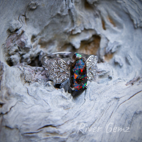 Vibrantly coloured dark opal approximately oval shaped claw set in white gold ring with six leaves adorned with diamonds each side of the opal.