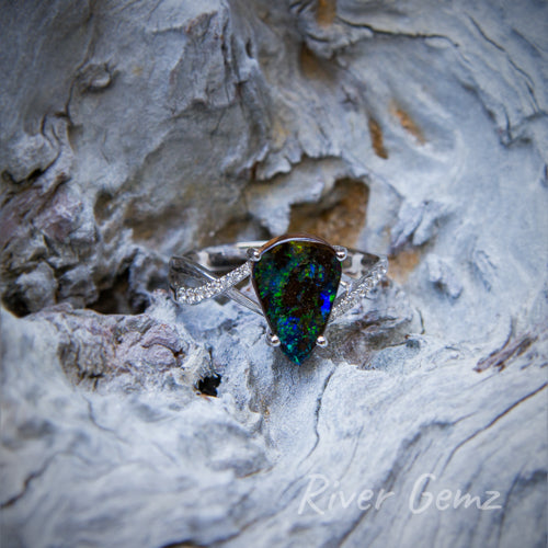 Dark green and blue opal claw set in white gold ring with a sequence of opals each side of the featured opal.