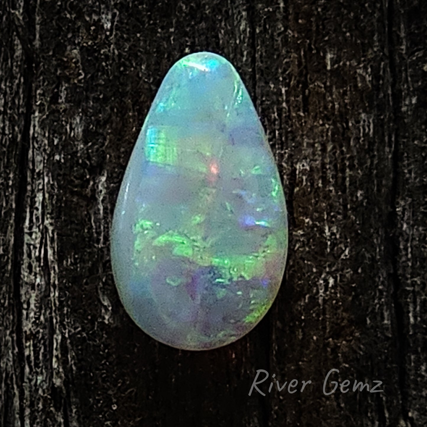 The tear drop shaped opal is resting on a dark brown grained piece of wood.