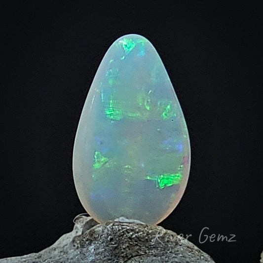 Large spheres of green and blue visible in the light opal. Opal is upright on a light-grey weathered piece of wood.