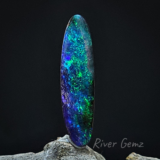 Long oval shaped opal full of colour photographed with a black back drop.