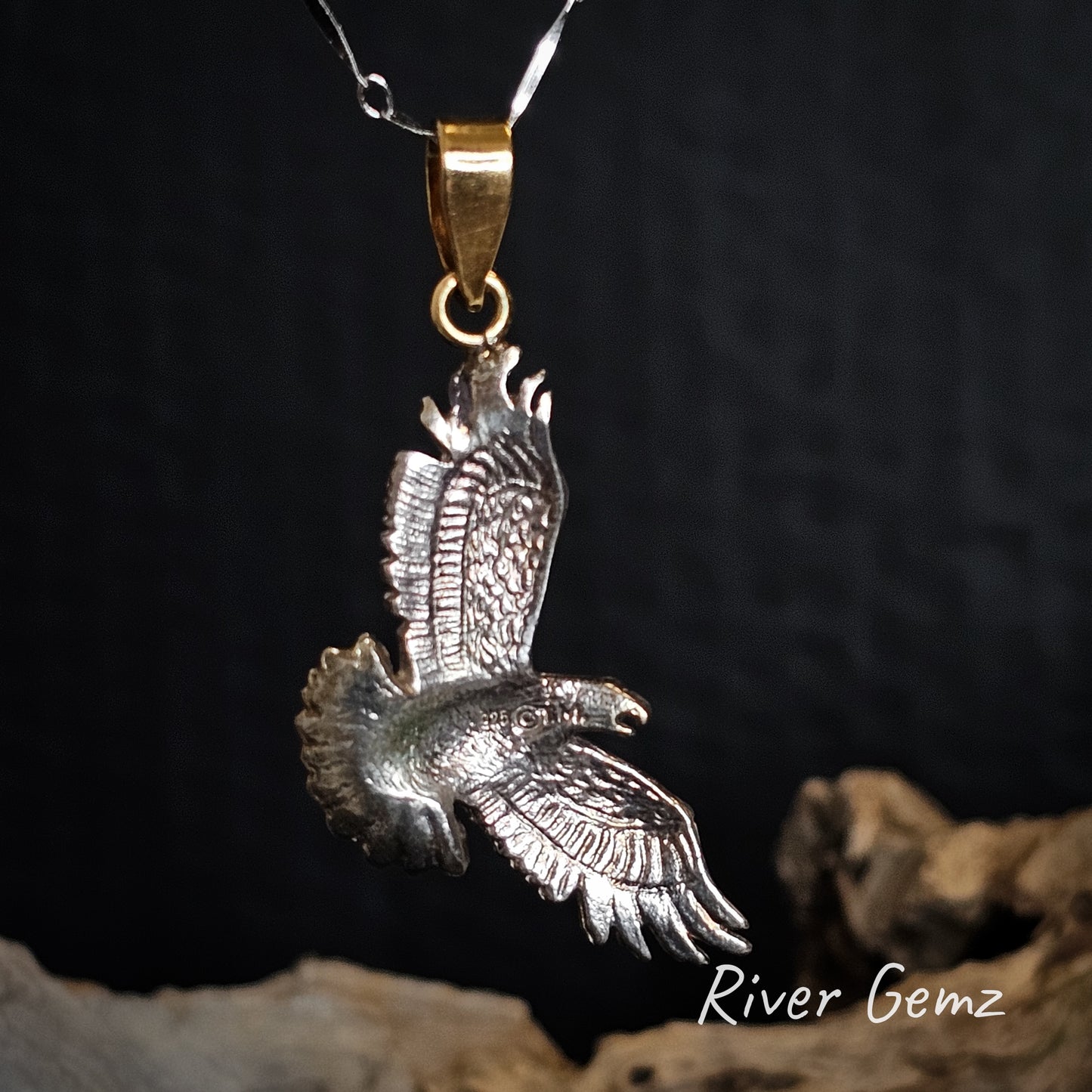 Back view of silver eagle pendant with gold bail on a dark background, branded 'River Gemz'.
