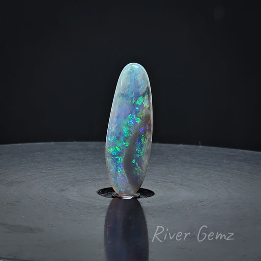 Oval shaped blue & green dark based unset opal standing upright.