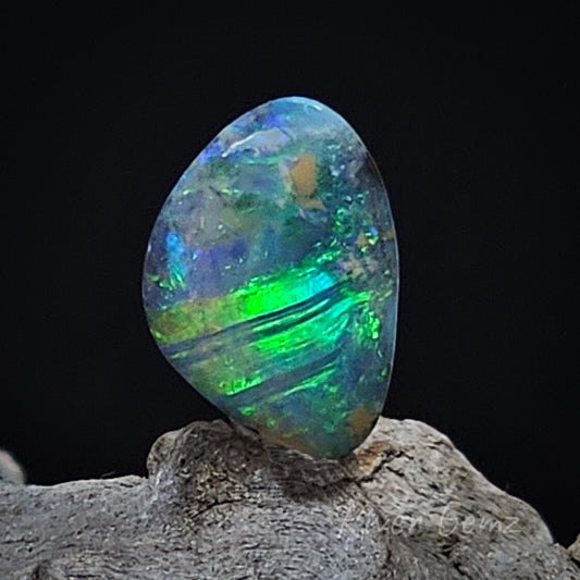 Approximately triangular shaped with rounded corners the opal is shown with a black background and wood grained base.