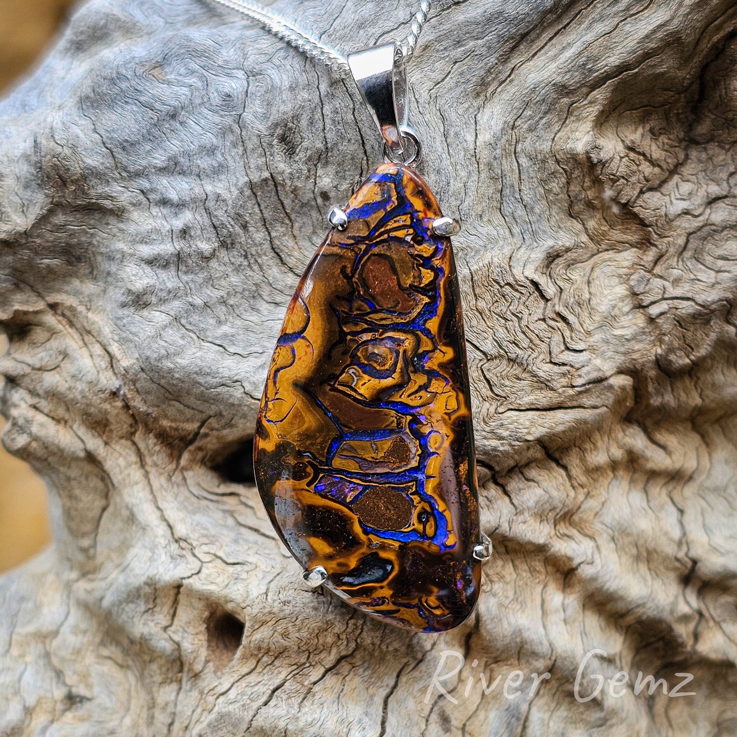 Close up photo of the pendant. Four claws secure the opal in the setting. The boulder opal is rounded-triangle shaped.