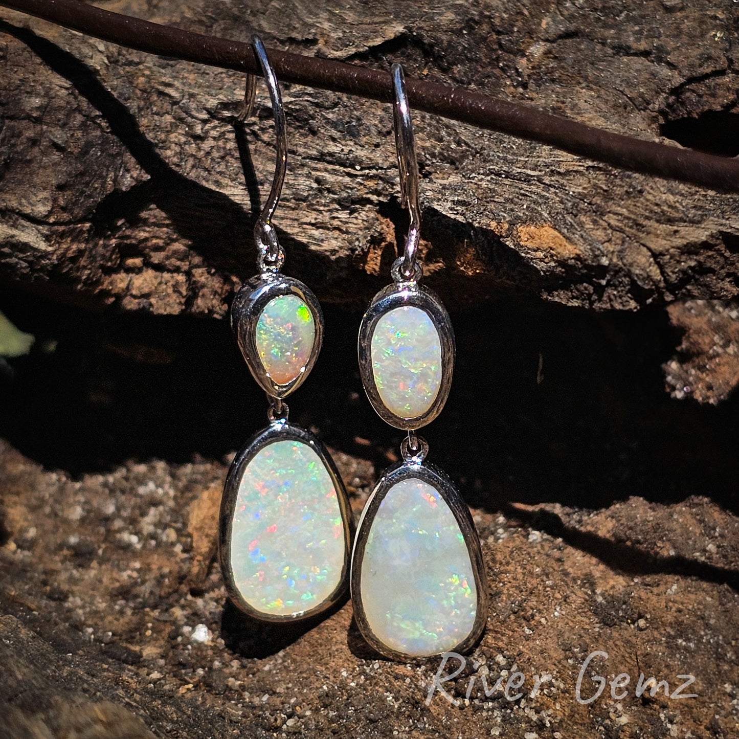 Two multi-coloured light opals in each earring. Eyelet connection between each besel set stone and also the hook of the earring for swivel action. White opals stand out against the dark wood grain back ground.