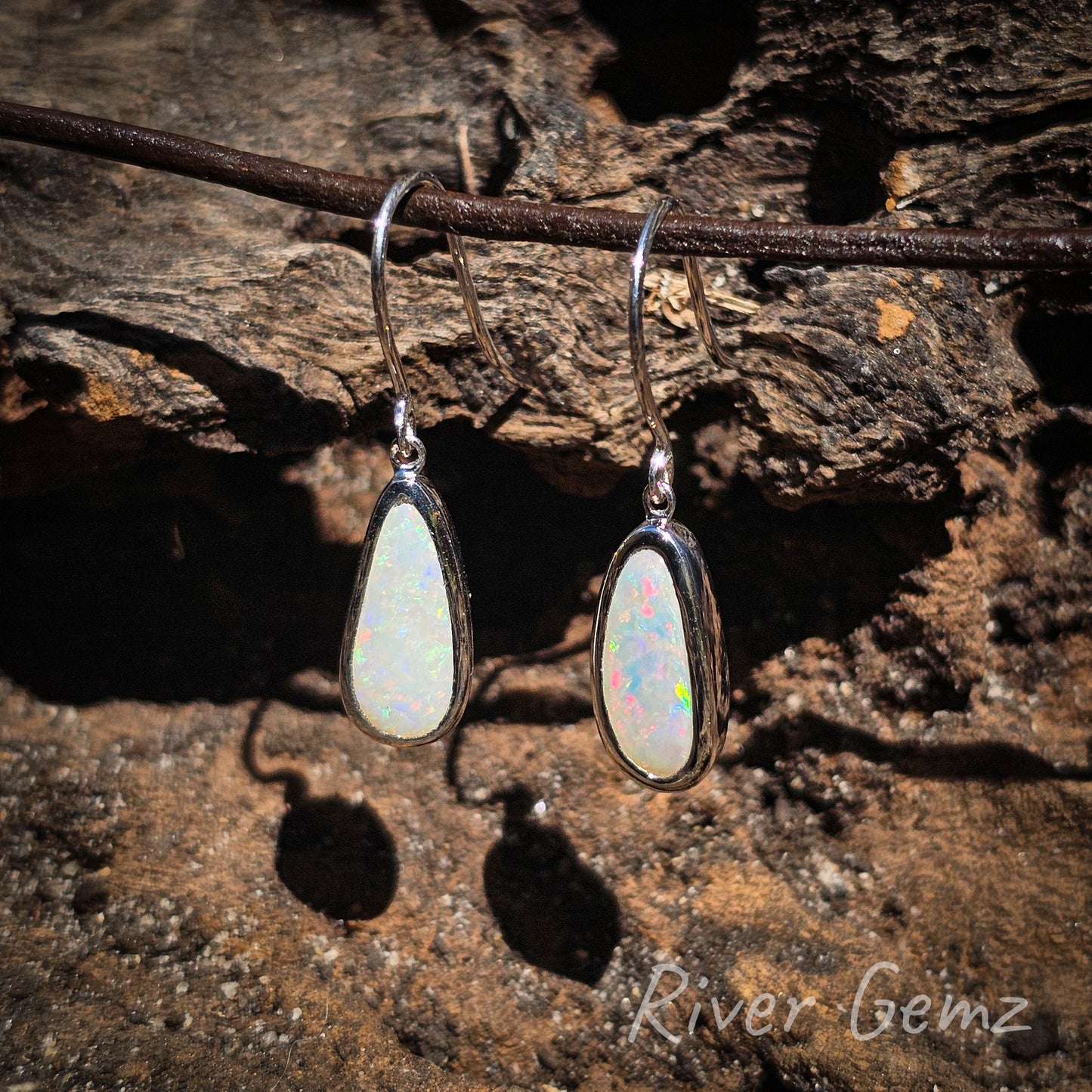 Multi-coloured light opals with eyelet connection to the hook of the earring. Good flashes of the rarer red colour in each opal. The white opal contrasts well against the dark wood grain background.