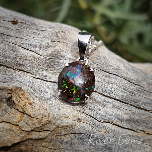 Small pendant with multi-coloured veins randomly distributed in the ironstone host rock. The matrix boulder opal is secured with 4 claws. The sterling silver bail is tapered and is almost half the size of the pendant. Earthy tones of the pendant show up against the light coloured drift wood.