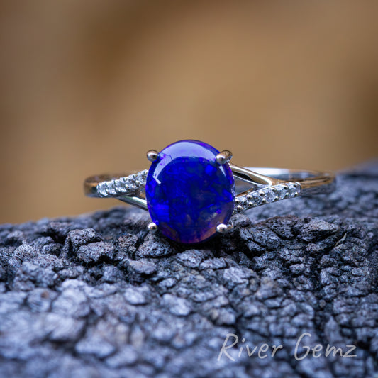 Four similar photos each showing oval shaped blue coloured black opal positioned on a dark grained piece of drift wood with a blurry brown back drop. This is a front view. 