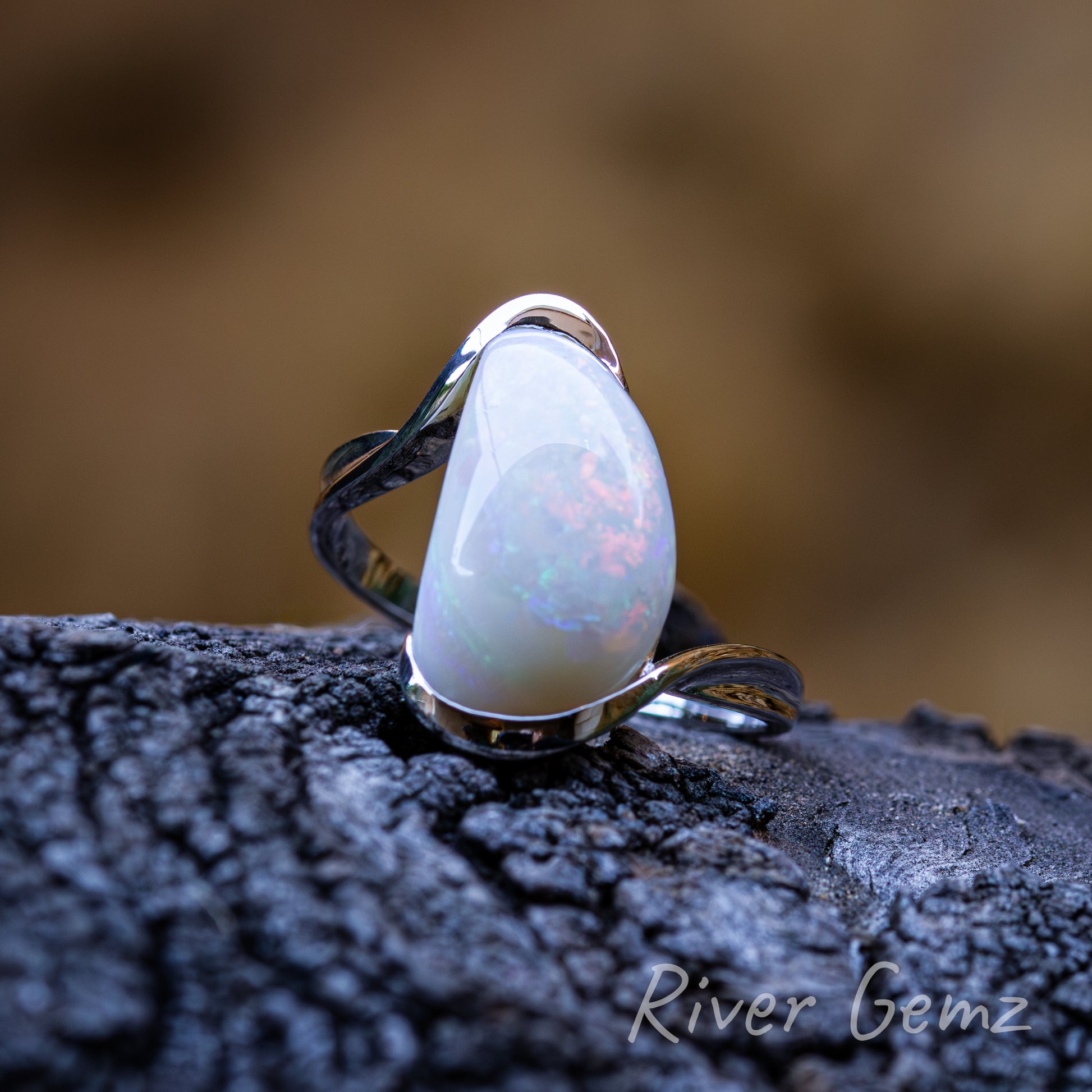 The large opal is bulging from the silver ring. Ring is photographed on dark grained piece of driftwood and the silver contrasts against the blurred light brown back drop.