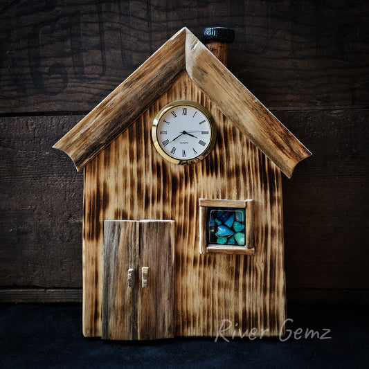 Cabin design wall clock with twin door on left and window on the right, v-shaped roof line frames the clock which is centred and at loft height. The blue-green opal slithers are within the window frame