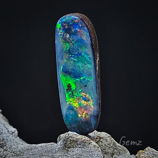 Approximately oval shaped solid unset opal shown against a black back drop. The ironstone host rock is visible in this view.