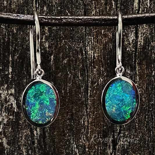 Green & blue oval shaped opals besel set in French hook earrings. All three photos shown the opals against a dark brown grained piece of wood.