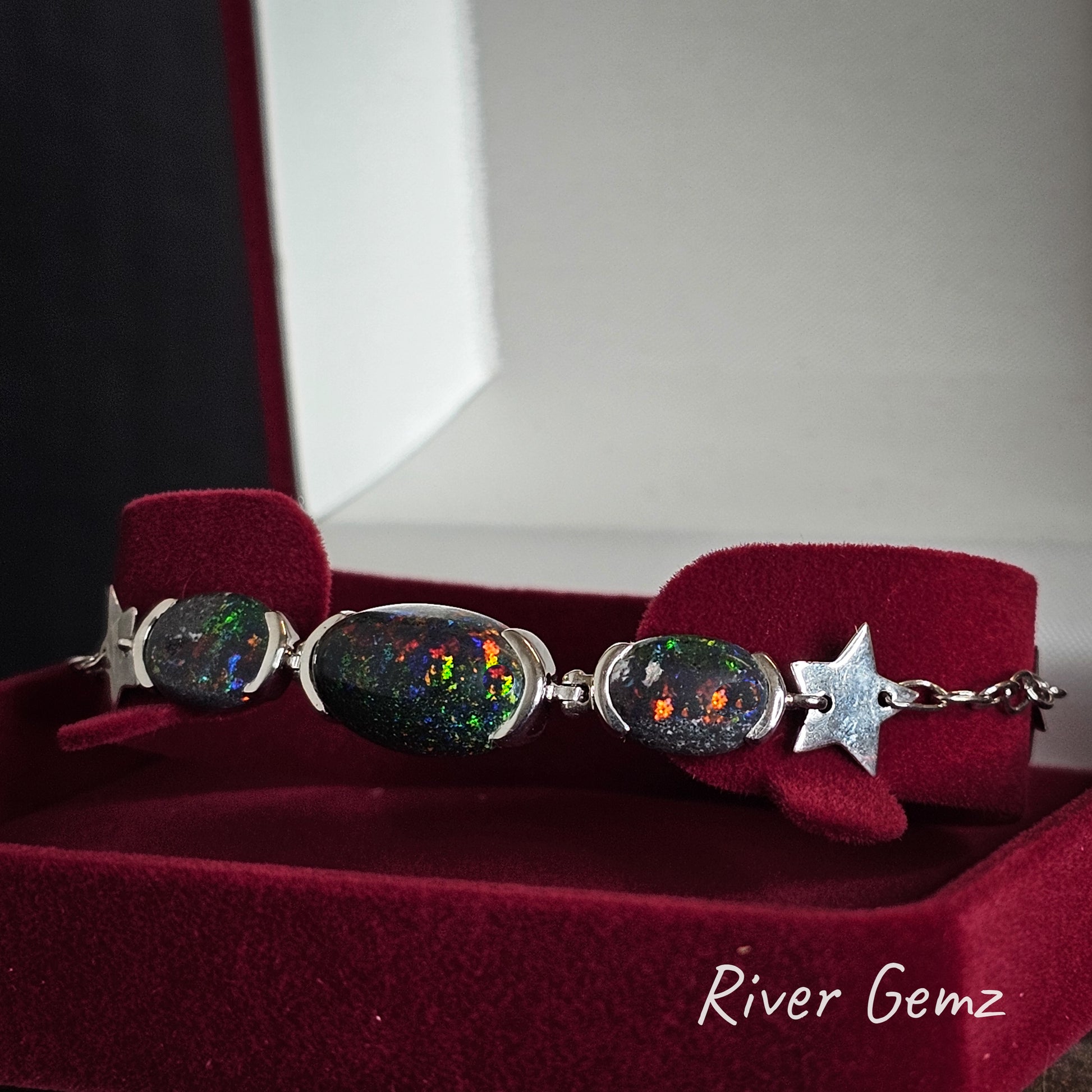Bracelet with star and oval dark opals in a red velvet jewellery box, branded 'River Gemz'.