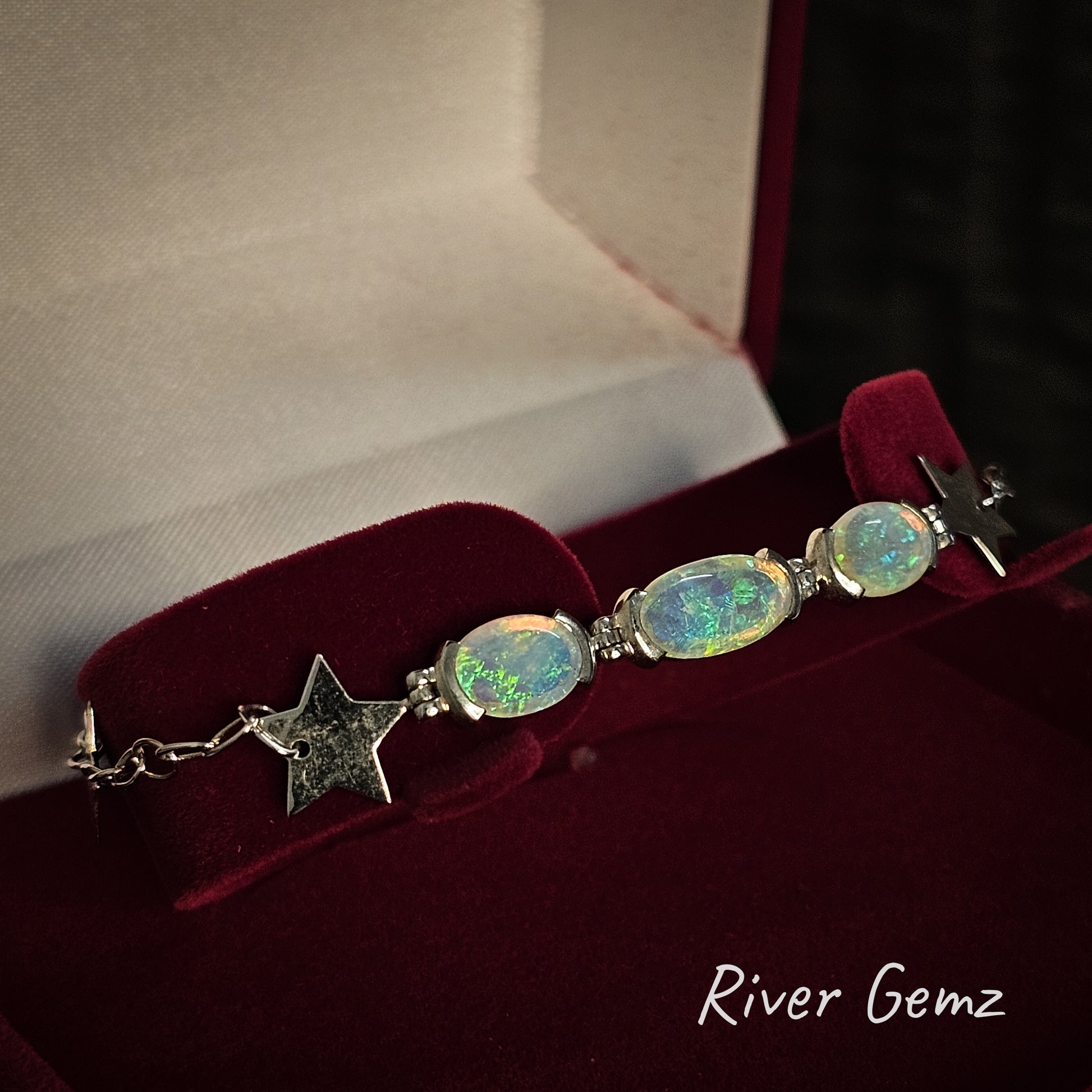 Three oval shaped crystal opals in a silver bracelet in a moroon velvet jewellery box.