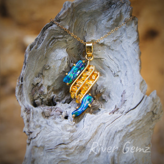 Two large blue-green dark opals claw set parallel outside two channels of gold nuggets in this gold pendant.