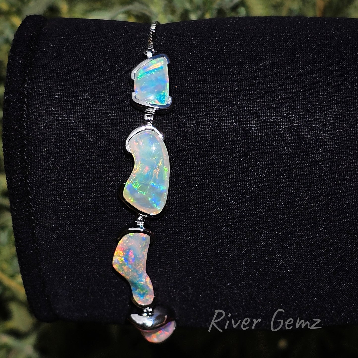 Modern style silver bracelet with 4 multi-coloured crystal opals pictured vertically.