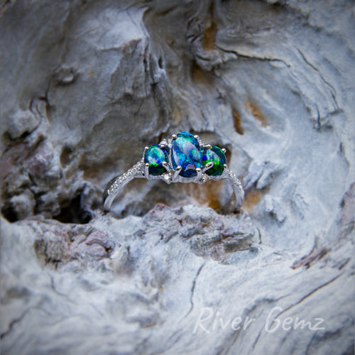 Three dark calibrated opals claw set in a white gold ring with multiple diamonds each side of the line of opals.