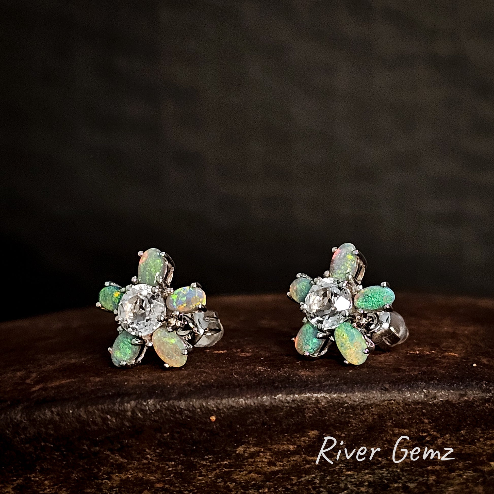 Pair of floral earrings with green gemstones on a dark background, branded 'River Gemz'.
