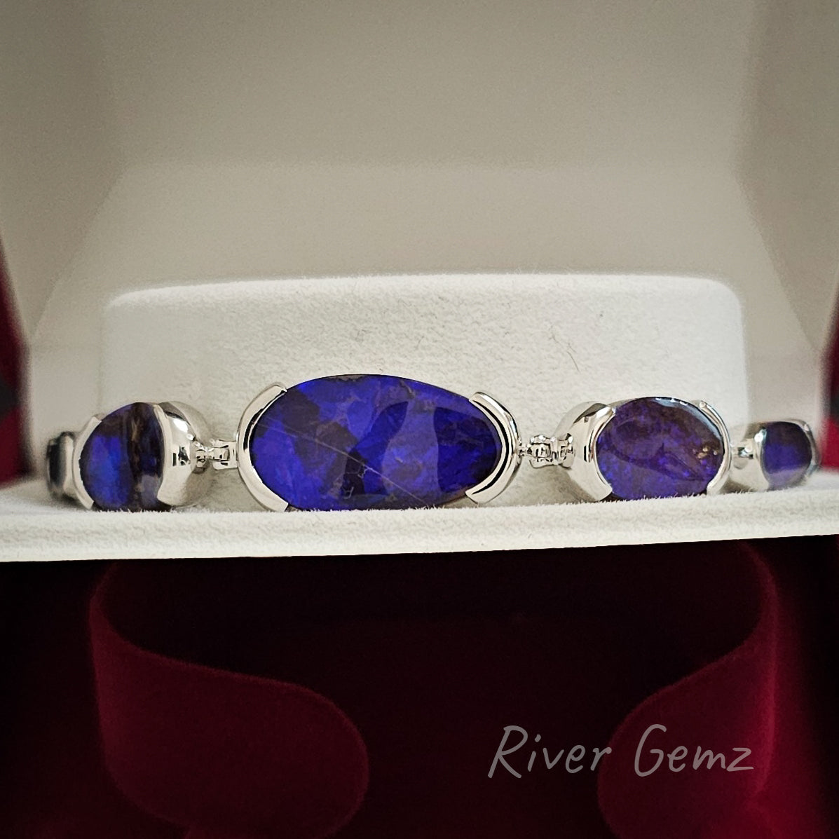 Five oval shaped dark blue opals partial besel set in silver bracelet shown in a bracelet box.