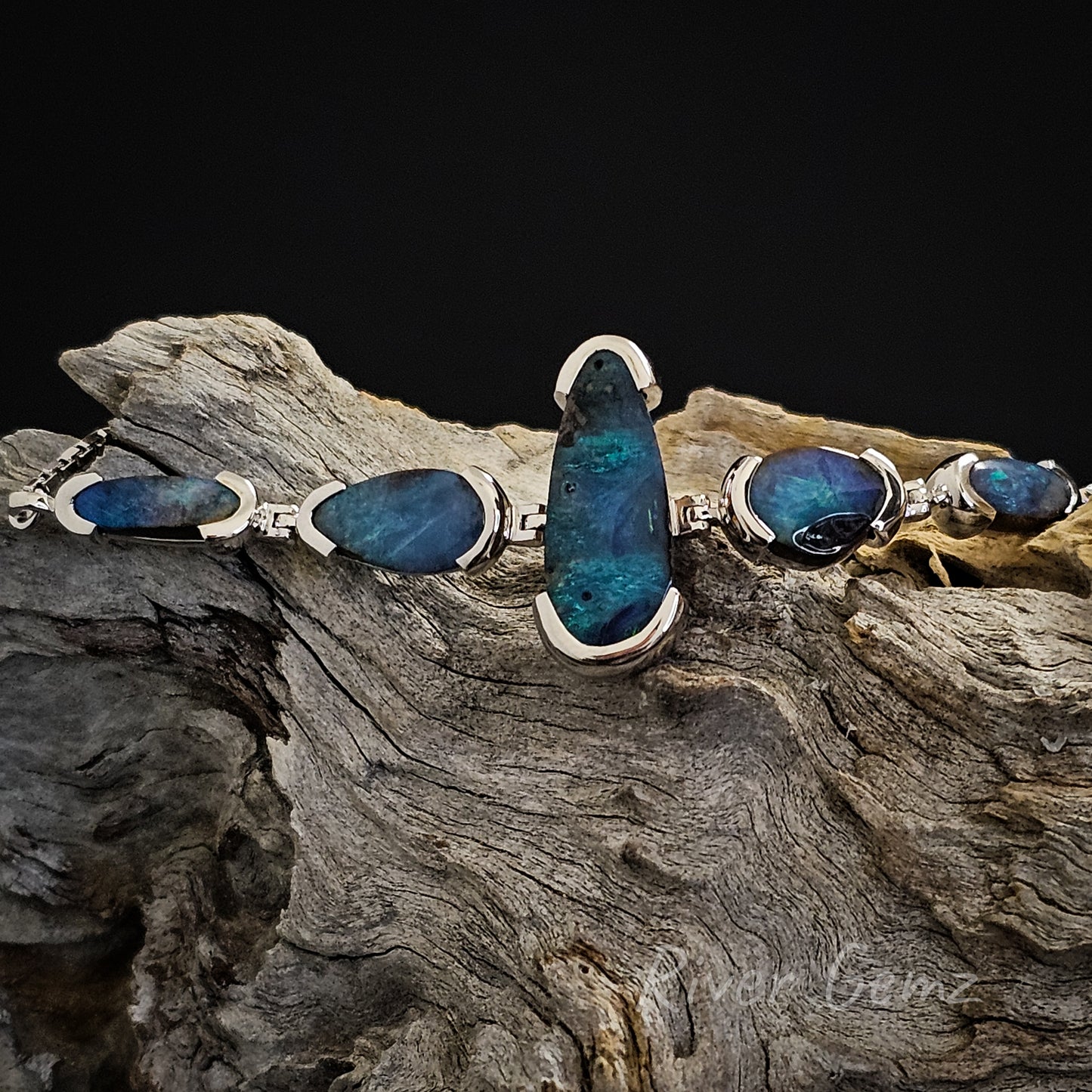 5 dark blue and green opals partial besel set in silver bracelet. 3 middle stones are tear drop shaped and the outer 2 are oval shaped.