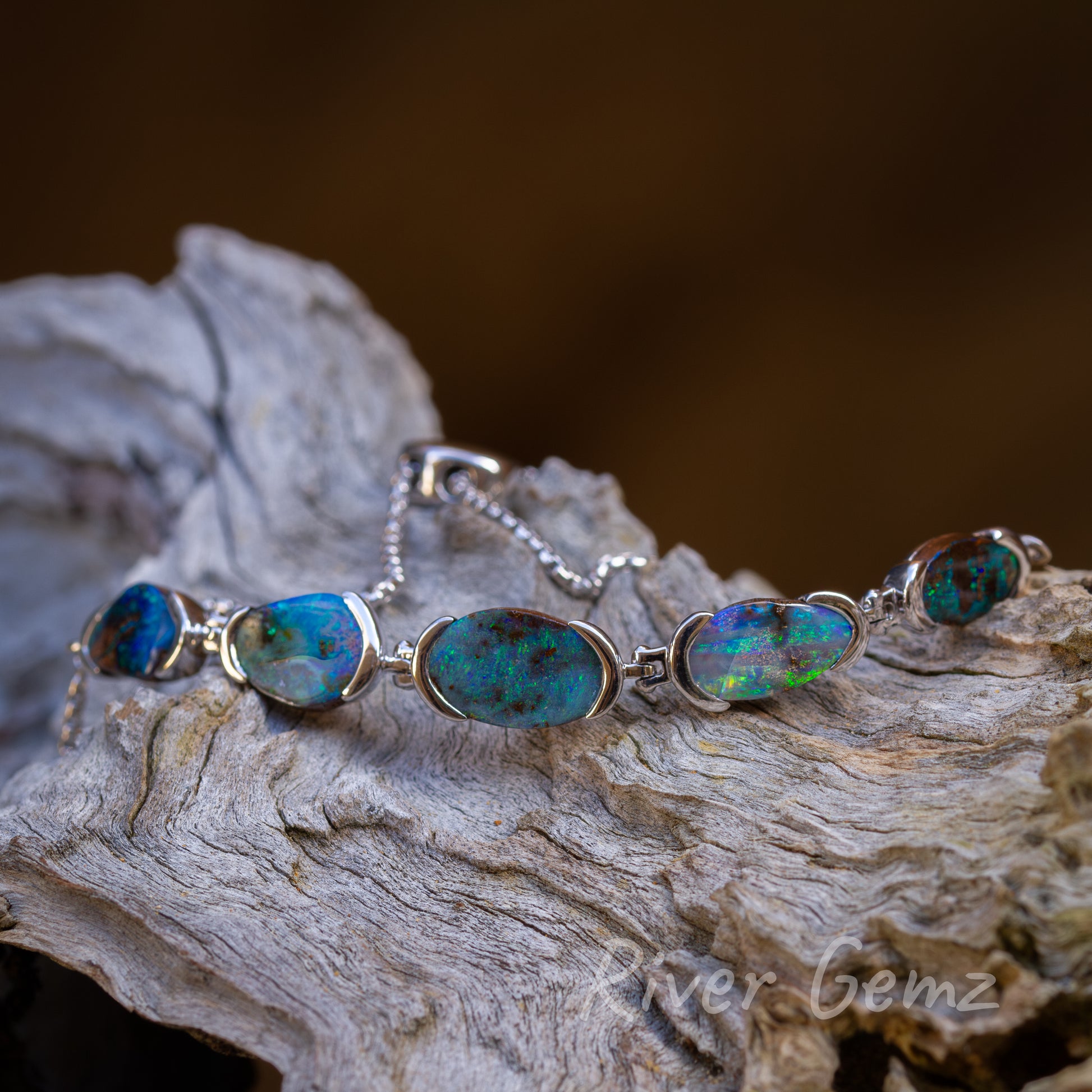 5 approximately equal oval shaped blue-green coloured opals partial besel set. Hinge connection between each opal. 