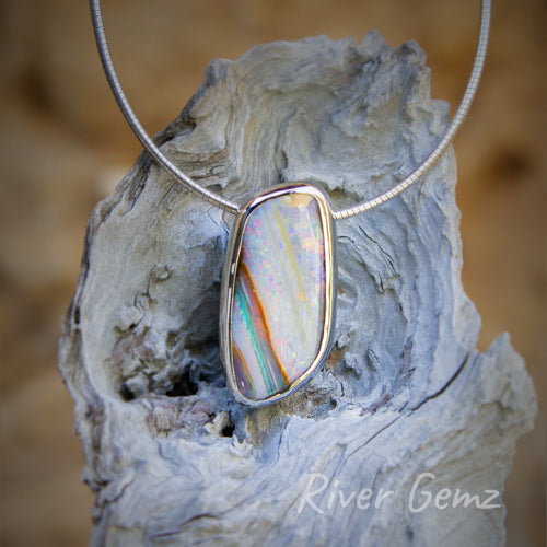 Large parallelogram-shaped opal with diagonal stripes of various colours besel set in a silver pendant.