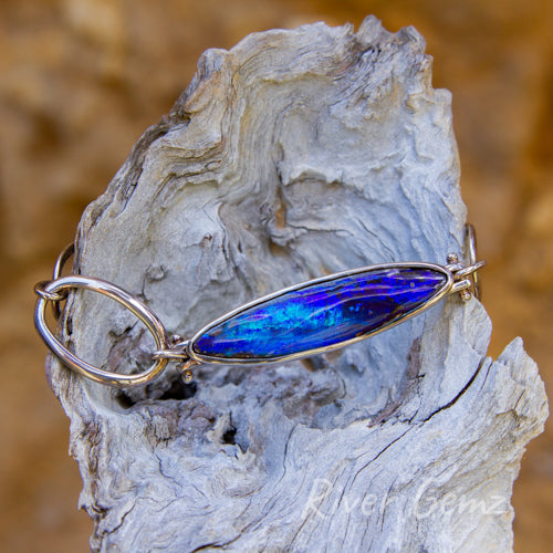 Long oval shaped dark blue opal besel set in silver bracelet with large oval shaped chain links to complement the opal setting.