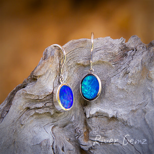 Oval shaped deep blue opals besel set in white gold hook earrings.