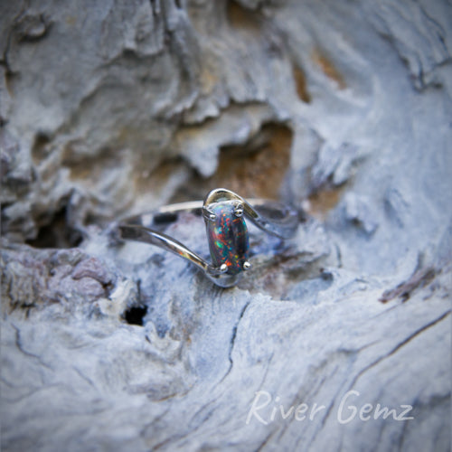 Multi-coloured oval-shaped dark opal in a modern design silver ring.