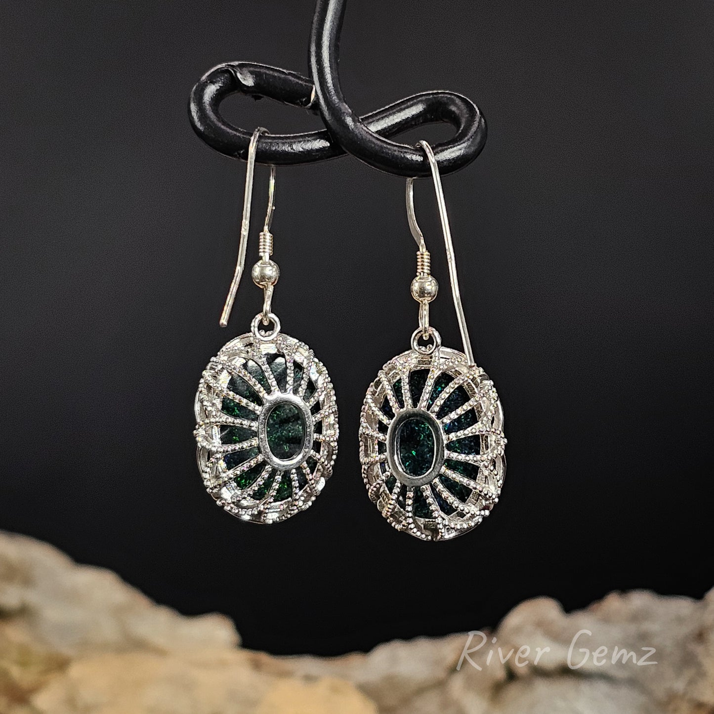 Rear view of French hook earrings show the ornate cage silver setting holding the oval shaped opals.