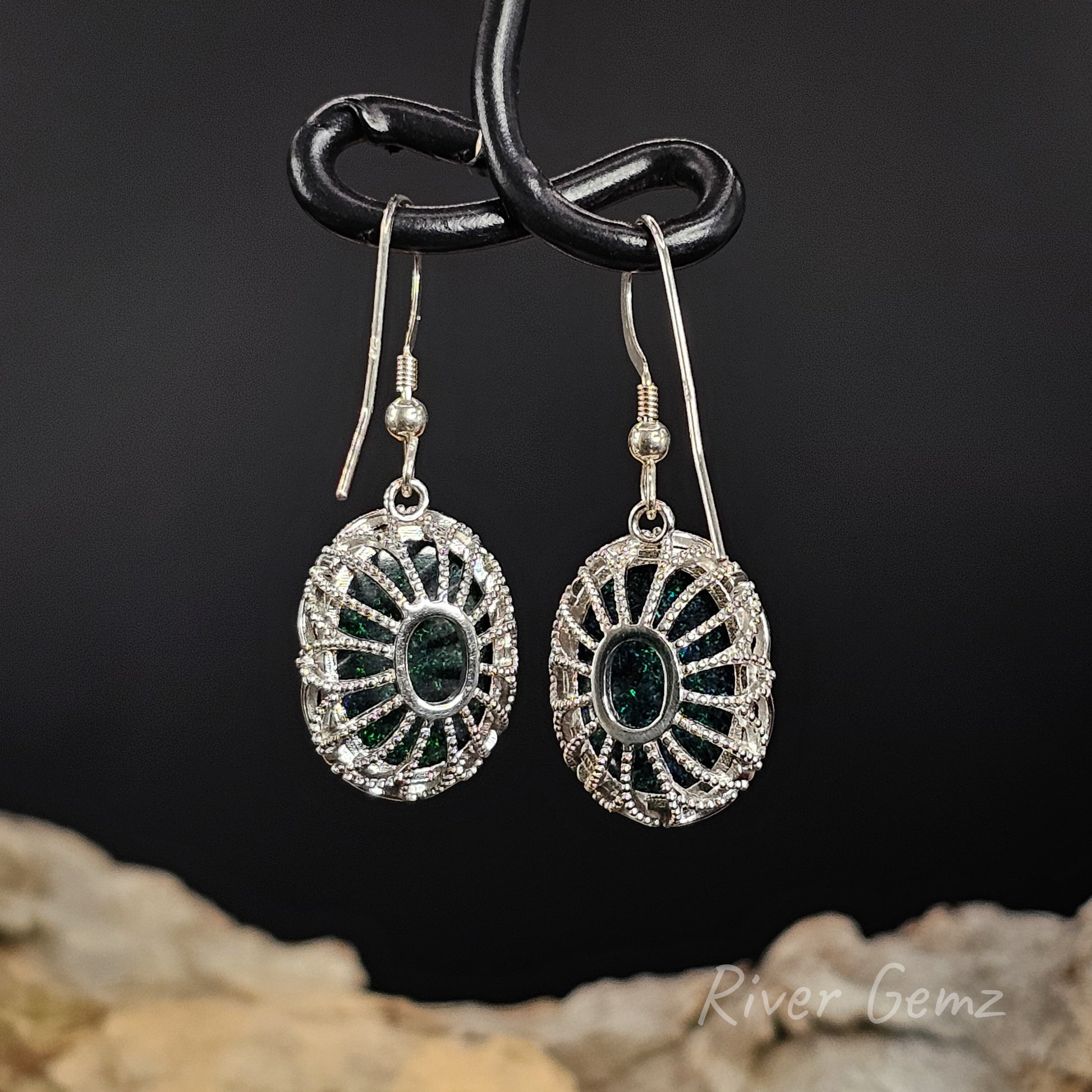 Rear view of French hook earrings show the ornate cage silver setting holding the oval shaped opals.