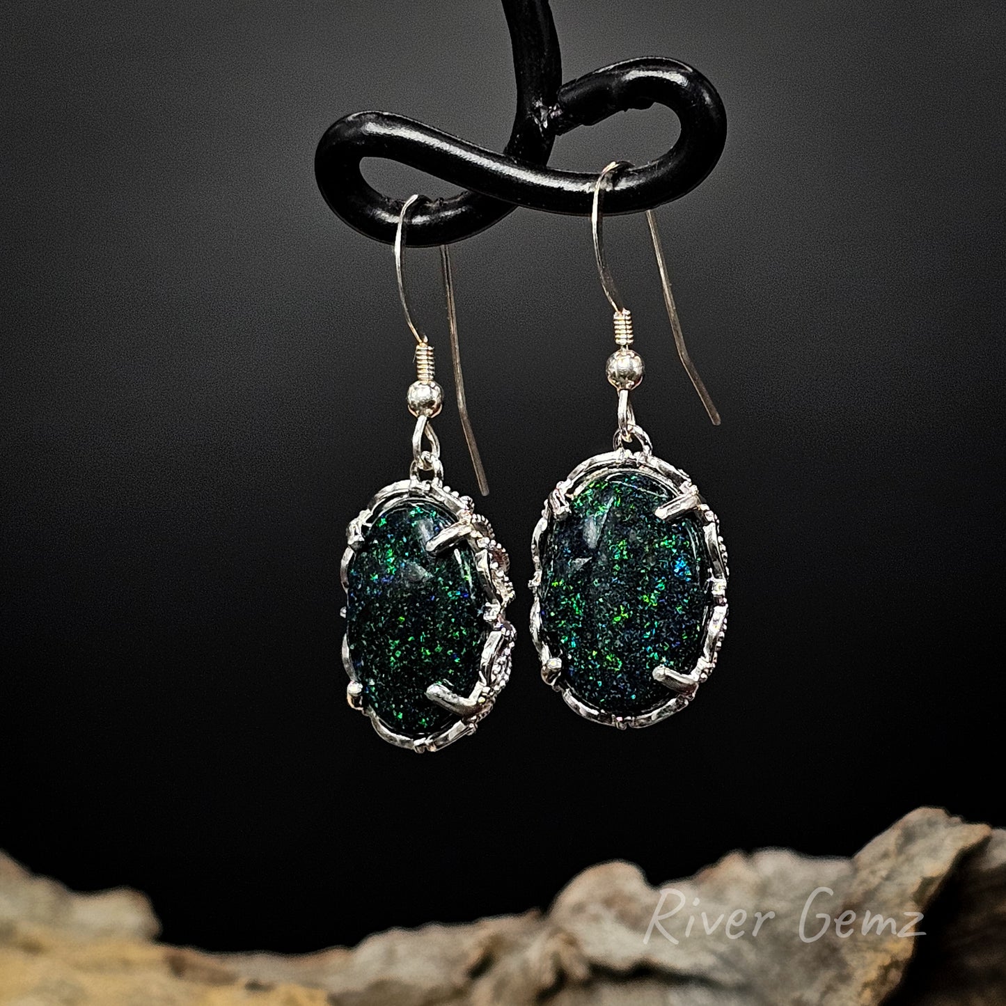 Dark green with some blue speckles in dark opals claw set in sterling silver hooks.