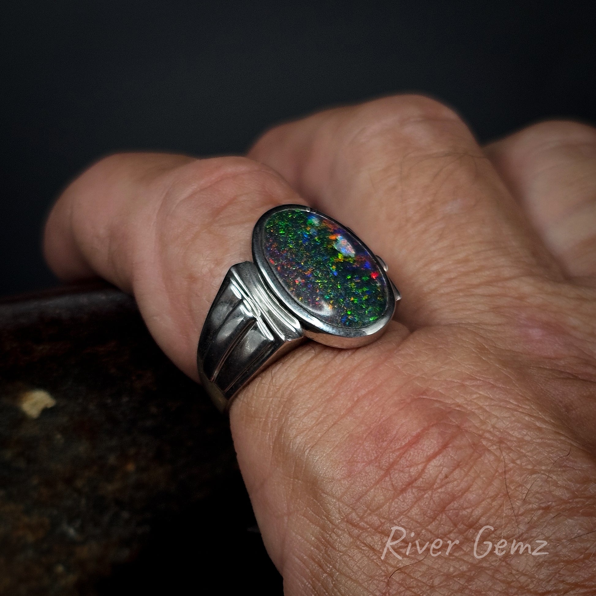Close-up of a hand wearing a silver ring with an opal stone, branded 'River Gemz'.