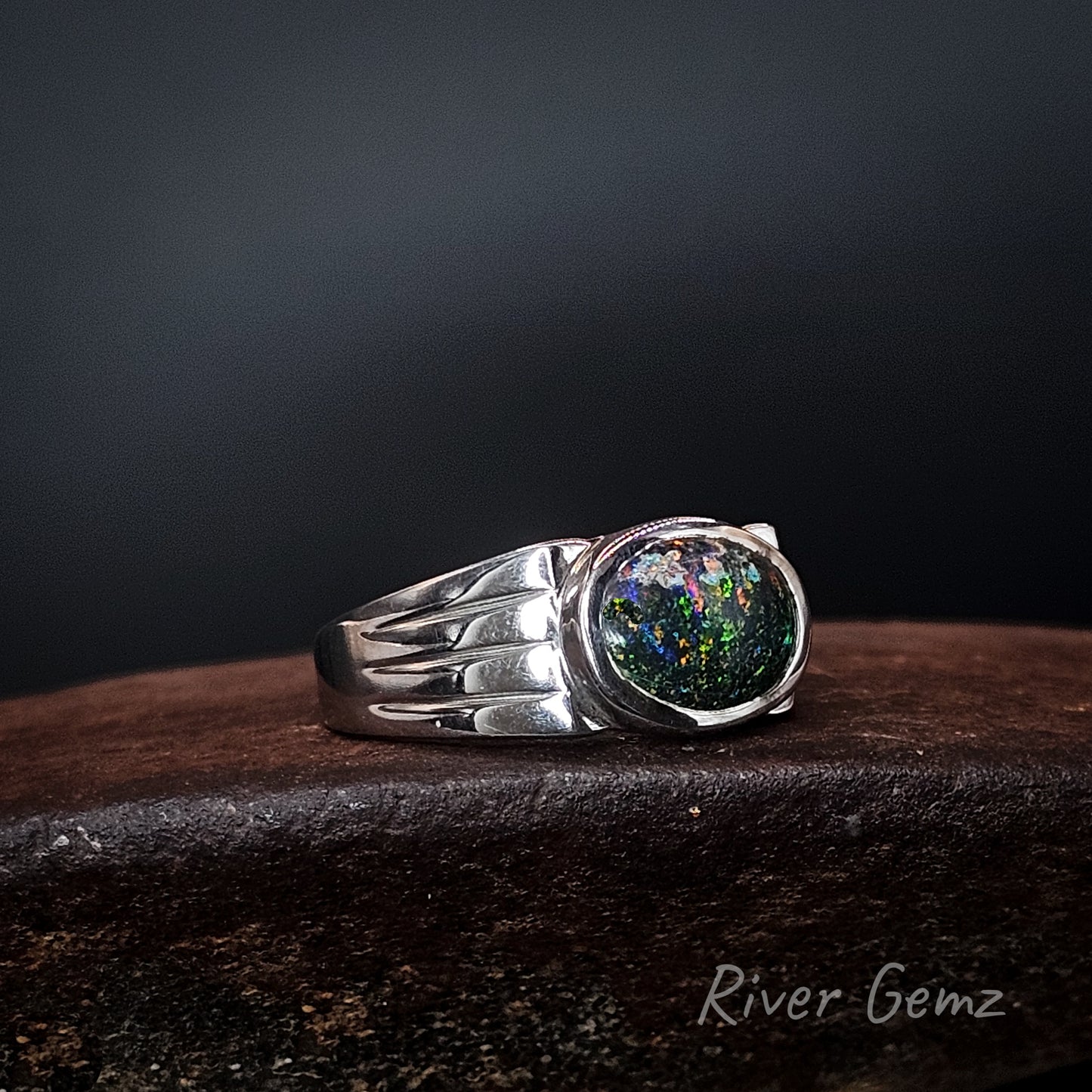 Pattern on the dark opal resembles a galaxy. The oval shaped stone is fully besel set in the sterling silver ring.