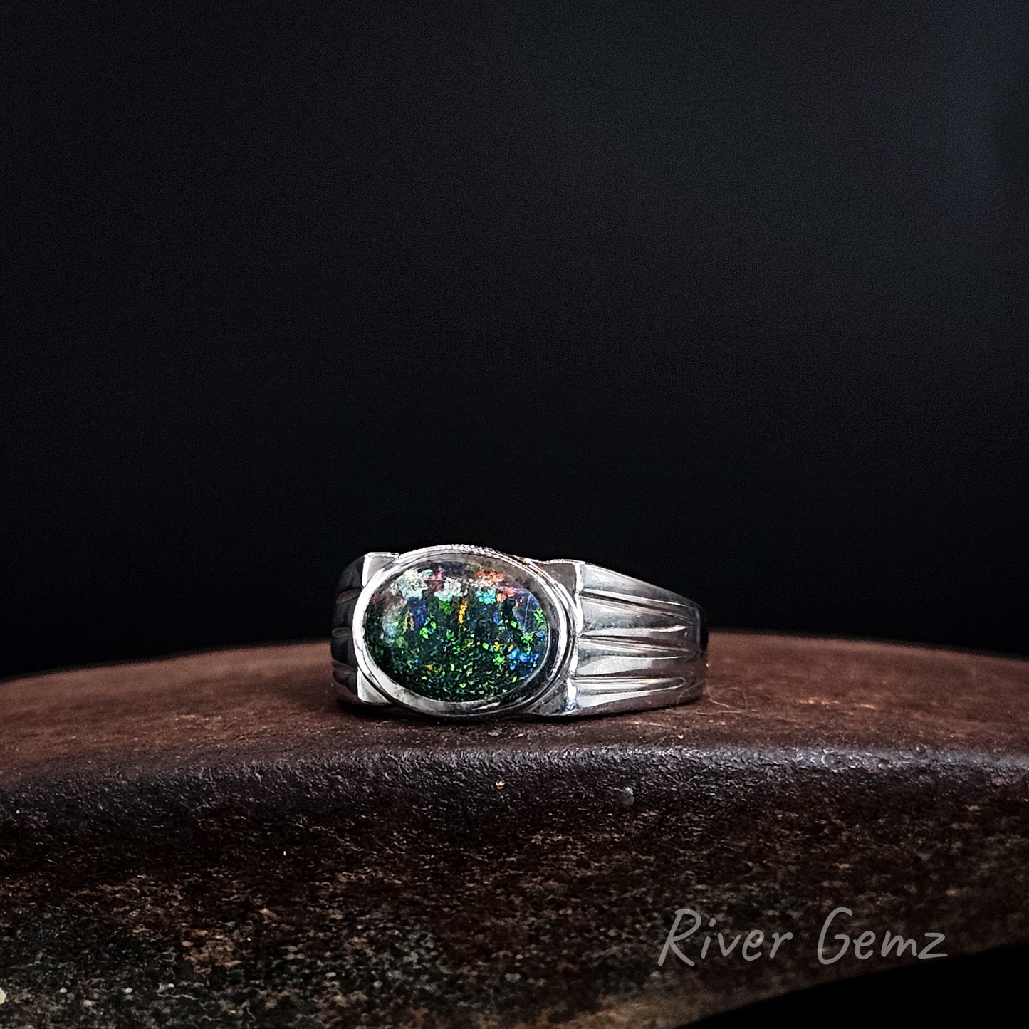 Oval shaped multi-coloured dark opal besel set in silver men's style ring.