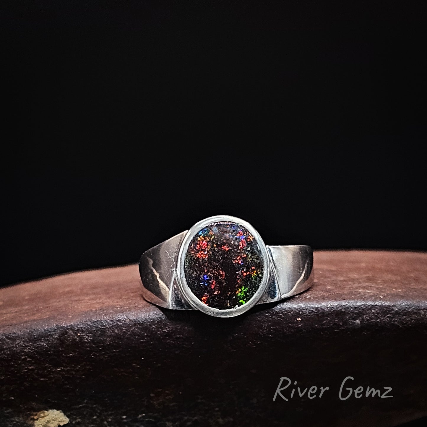 Oval shaped multi-coloured dark opal besel set in silver ring.