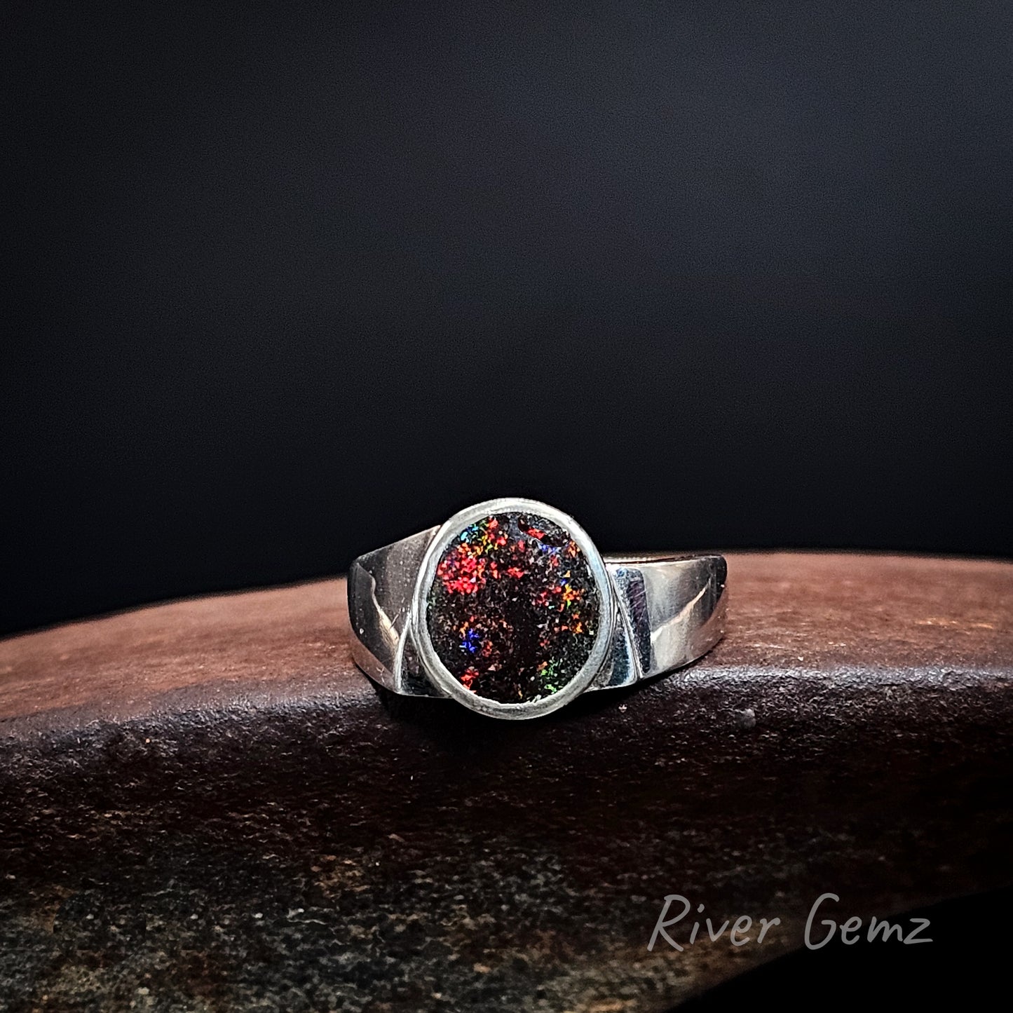 Dotted colours on a dark base tone opal set in a silver ring with unequal shoulders.