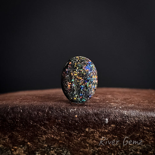Multicolored speckled loose matrix opal on a dark background with 'River Gemz' branding.