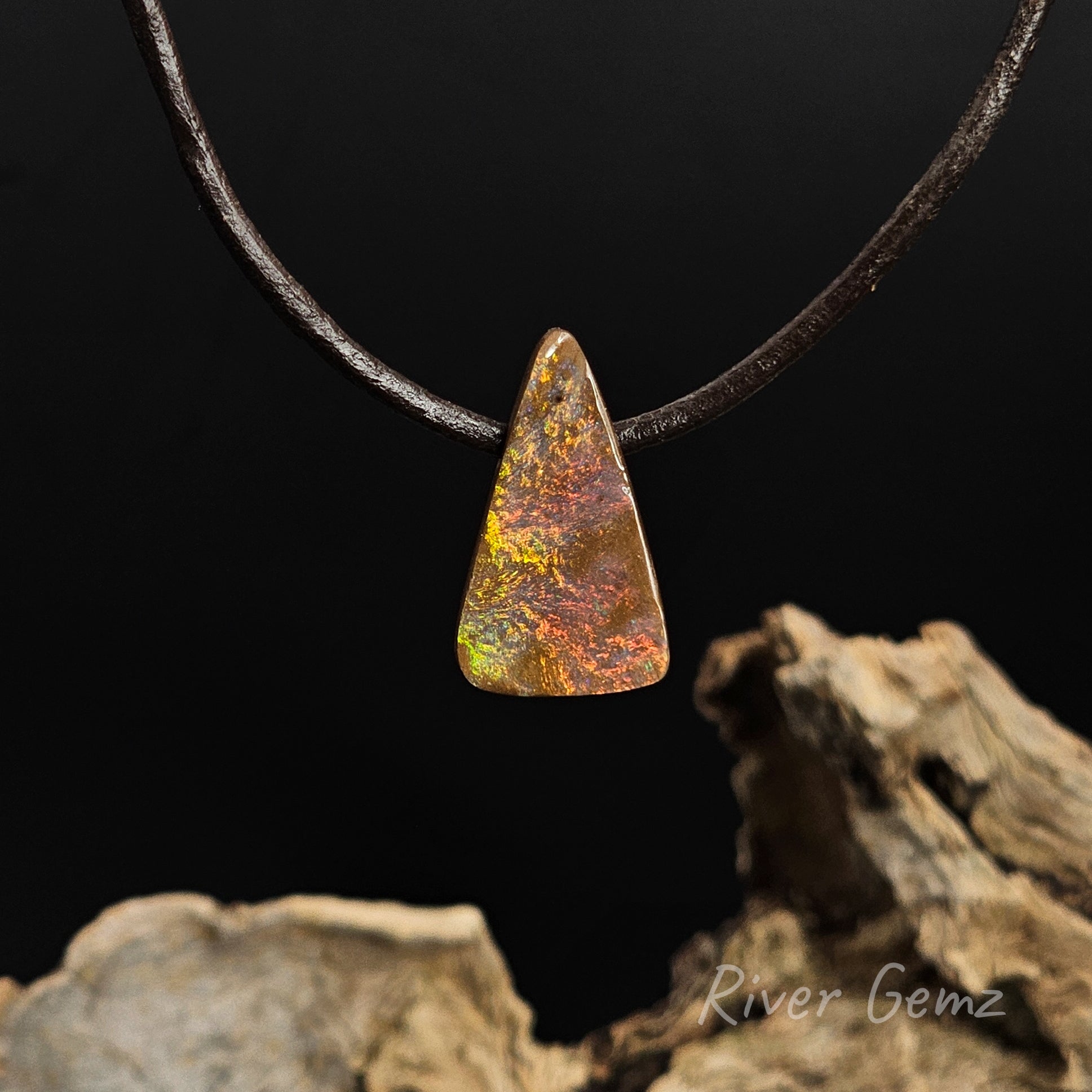 Stunning vibrant fire-like colours in a boulder opal necklace on a black background with 'River Gemz' branding in the bottom right hand corner.