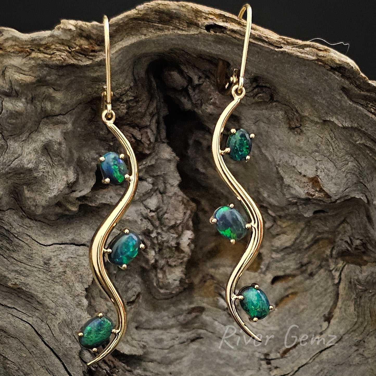 Stylish long yellow gold hook earrings with 3 dark oval shaped opals in each earring.