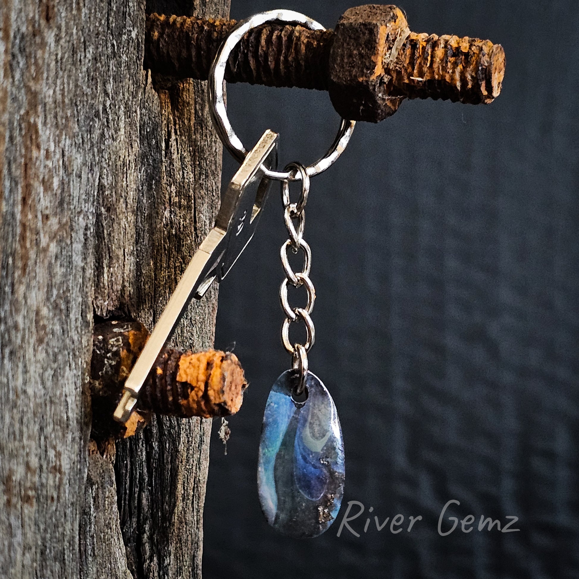 Approximately oval shaped boulder opal  with swirls of different shades of blue on silver coloured key chain.