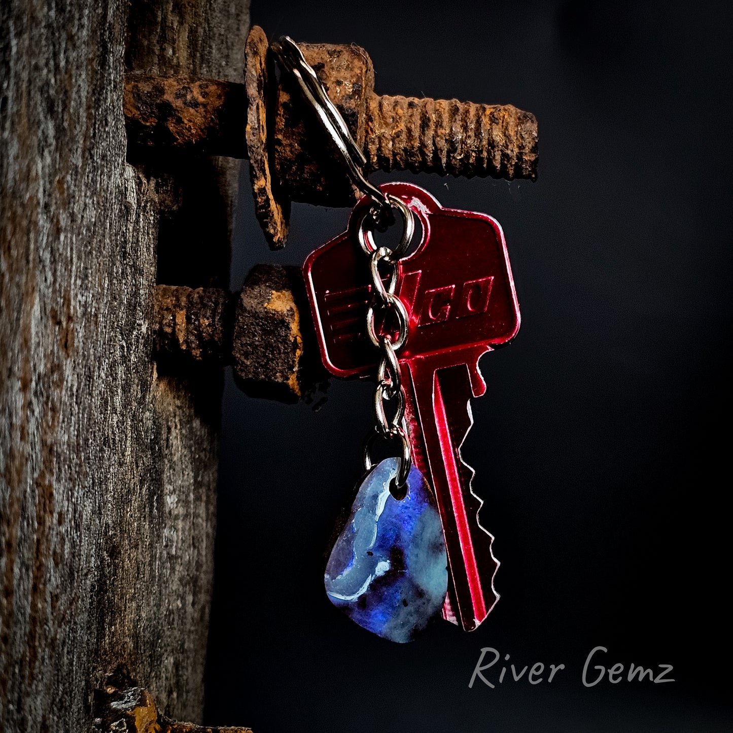 Keychain with a key and blue stone on a dark background, featuring the brand 'River Gemz'.