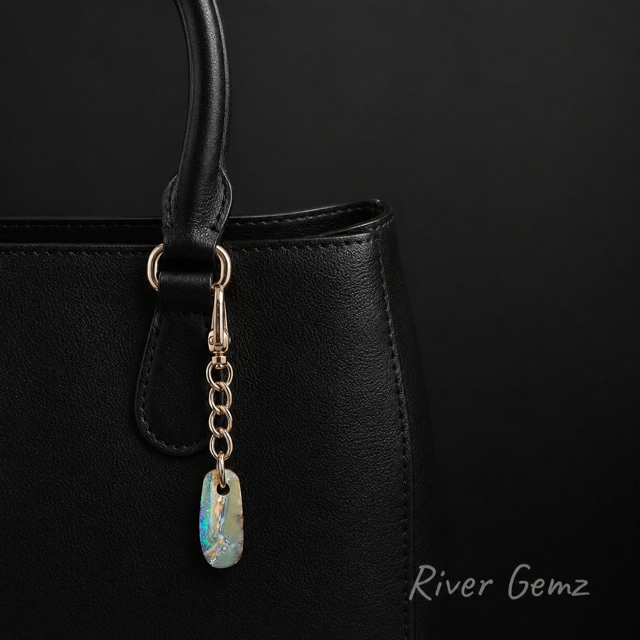 Black handbag with a bag charm featuring a natural opal stone on a black background, branded 'River Gemz'.