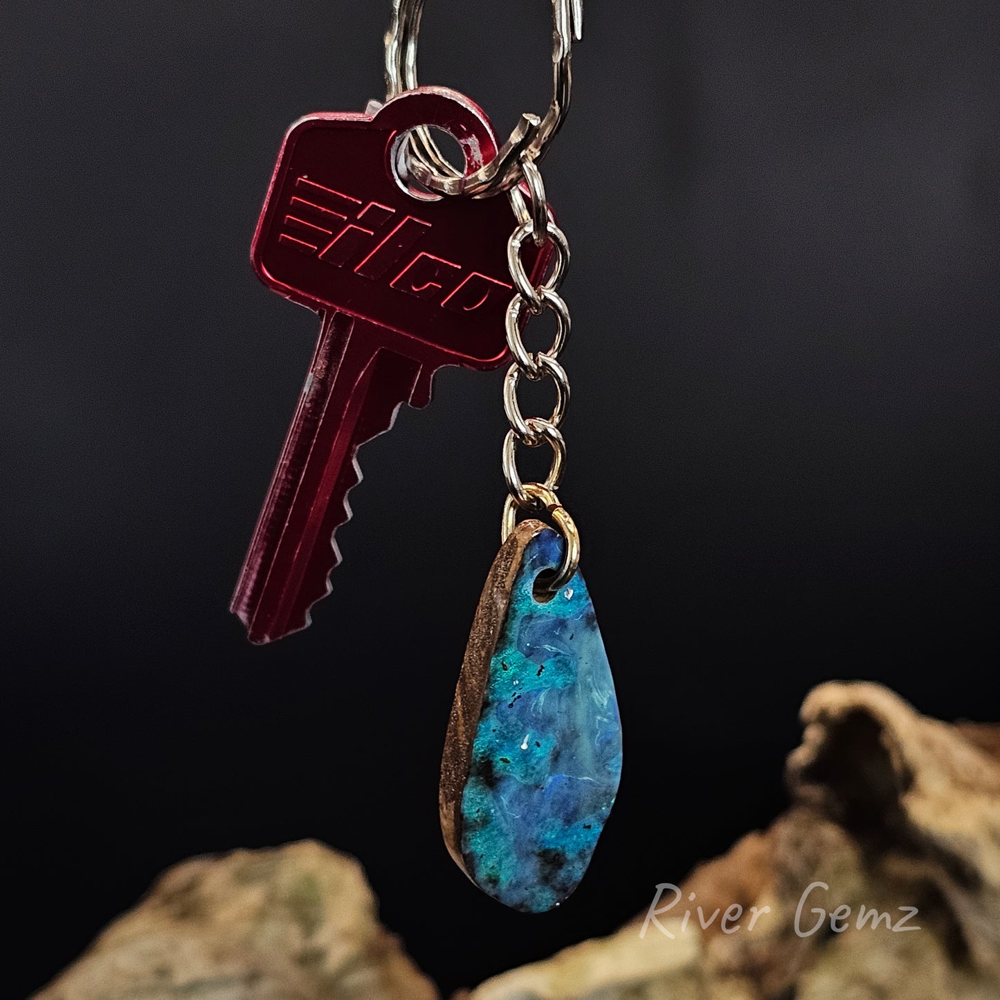 Keychain with a red key and blue teardrop boulder opal on a dark background
