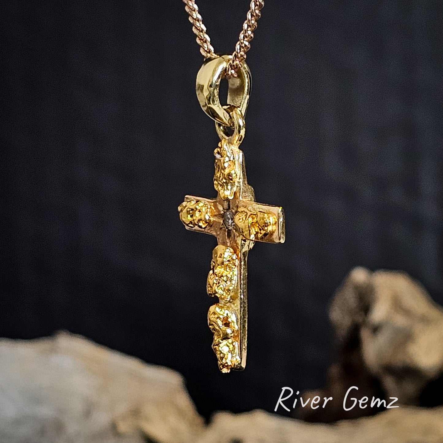 Slightly skewed view of the gold and gold nugget cross pendant necklace on a dark background with 'River Gemz' branding.