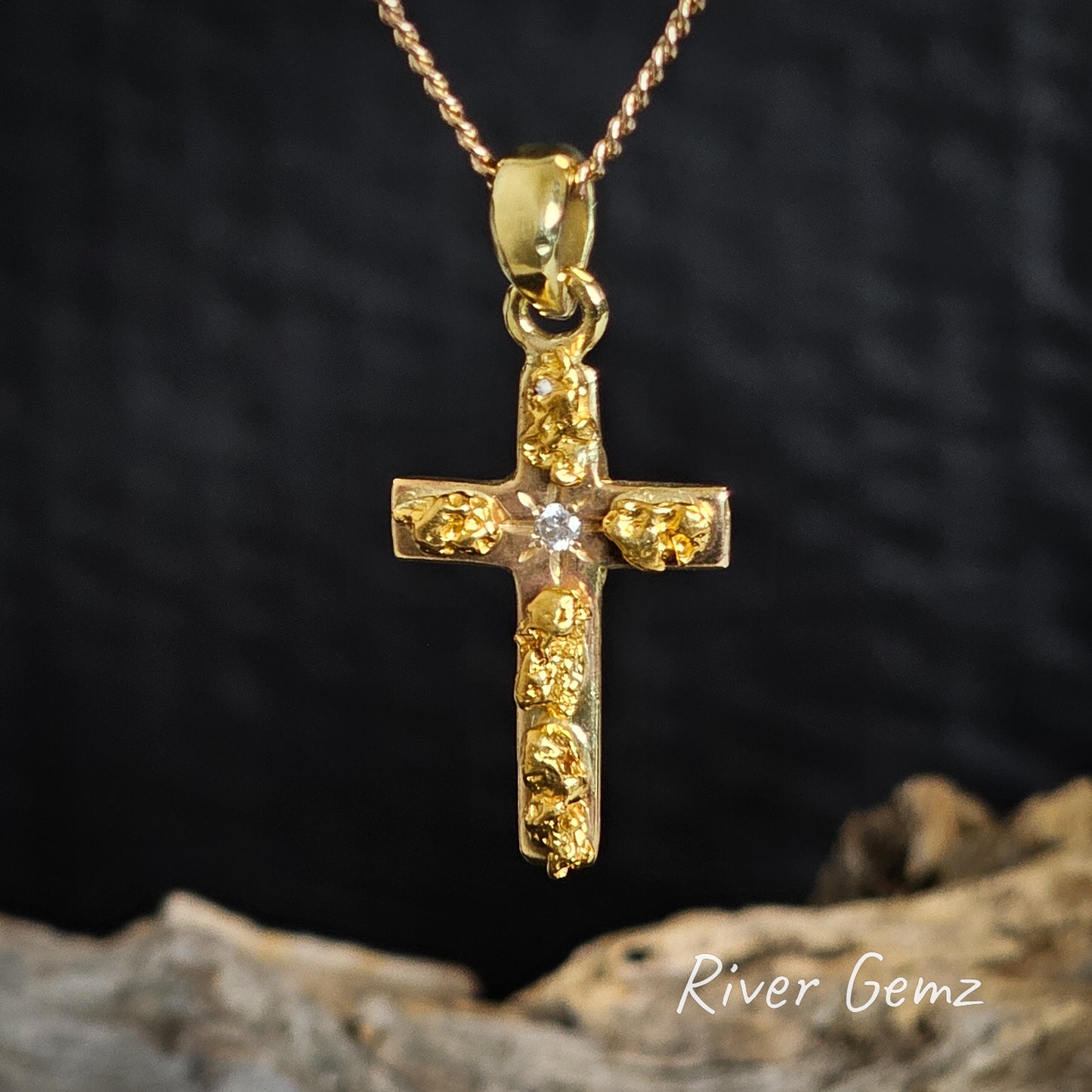Gold cross pendant with embedded nuggets and a diamond on a dark background, featuring 'River Gemz' branding.