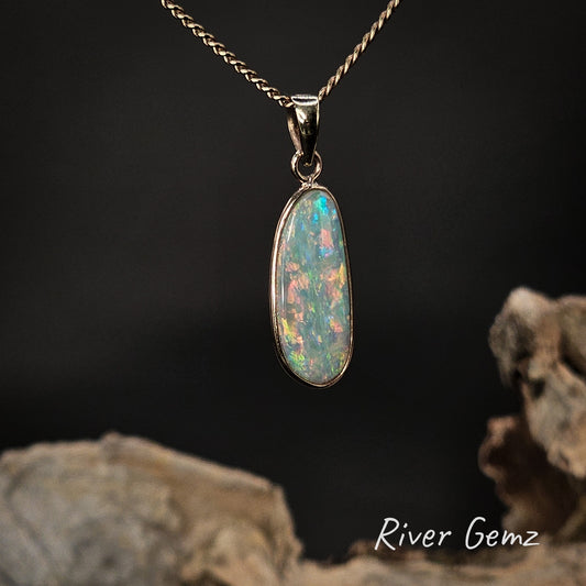 Multi-coloured crystal opal besel set in yellow gold necklace on a dark background with 'River Gemz' branding.