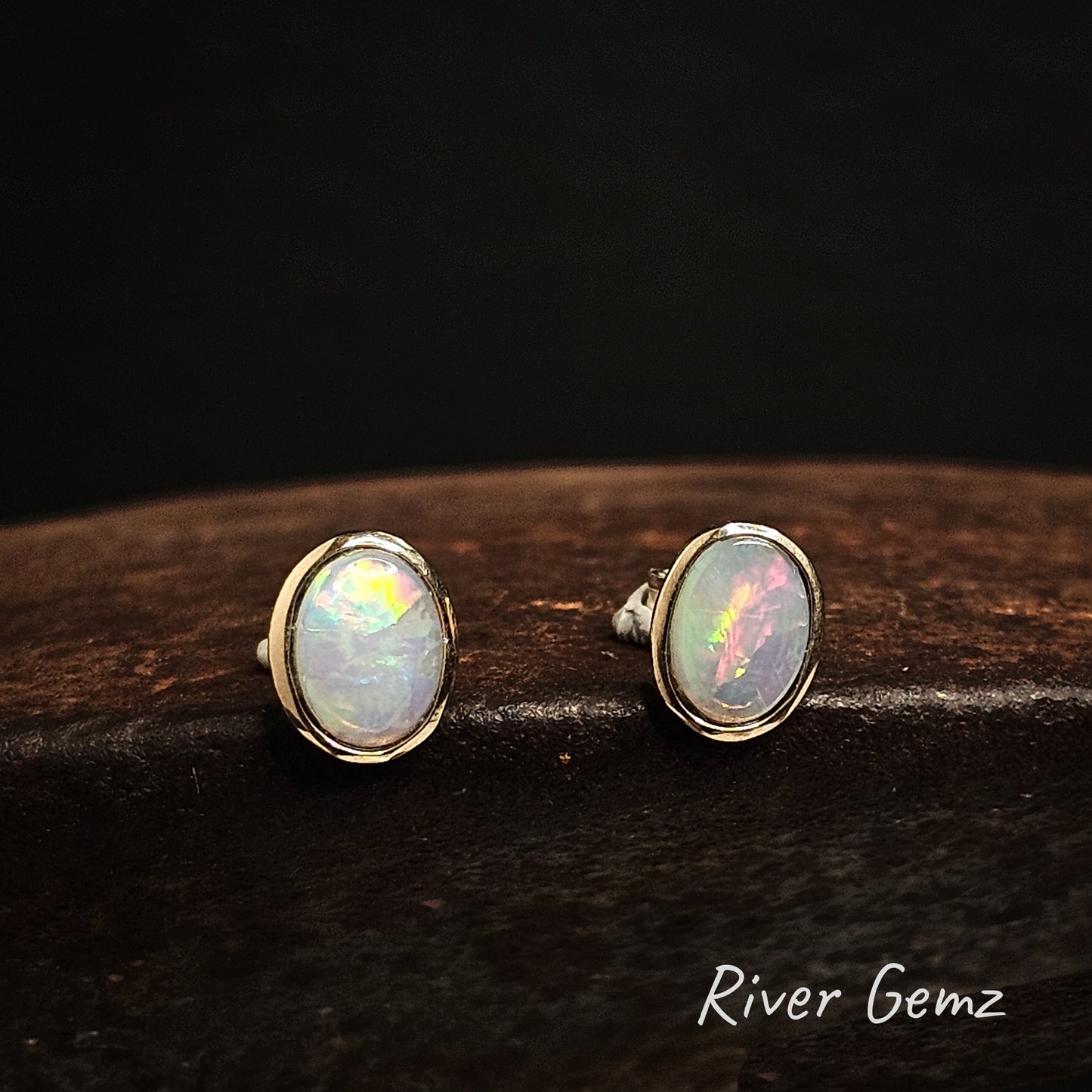 Oval shaped multi-coloured light opals besel set in yellow gold studs.