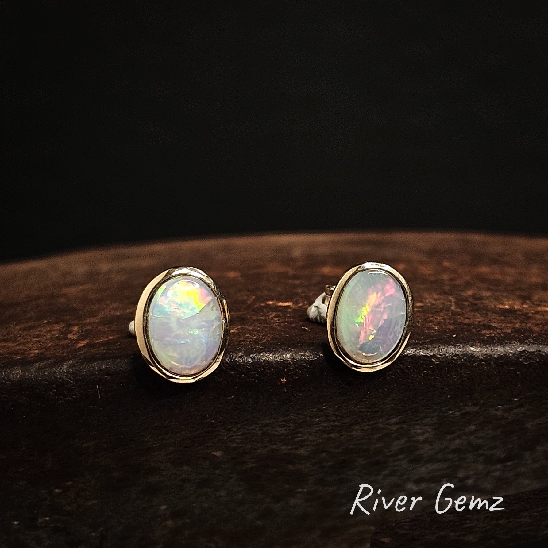Oval shaped multi-coloured light opals besel set in yellow gold studs.
